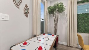 Ein Zimmer mit Kicker, einem Sessel, einer Pflanze und einem Vorhangfenster.