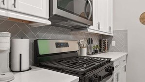 A kitchen with white cabinets, a stainless steel microwave, a gas stove, and a coffee maker.