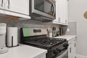 A kitchen with white cabinets, a stainless steel microwave, a gas stove, and a coffee maker. - Tropical Jungle Home Escape & Retreat (Houston)
