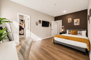 Quarto com cama, escrivaninha, cadeira, televisão e obras de arte na parede.