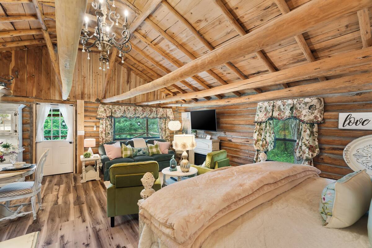 Interior de una cabaña de troncos con una cama, un sillón verde y un televisor.