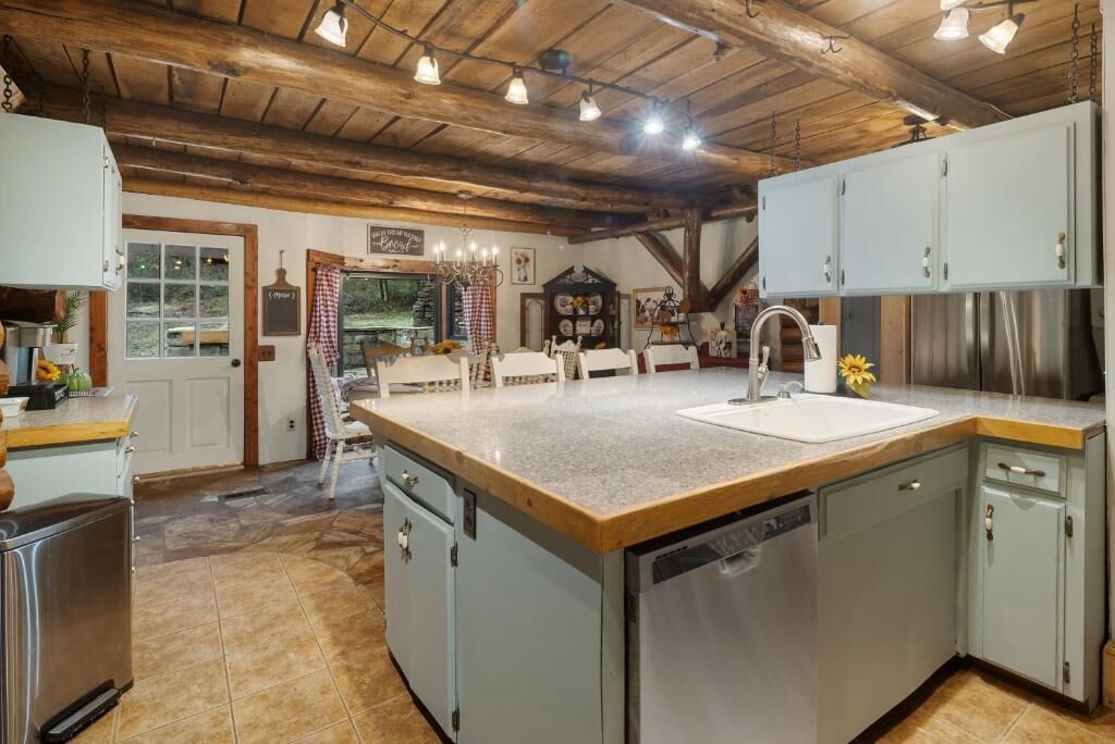 Una cocina con una isla central, un fregadero y un lavavajillas. Hay armarios, una encimera y un techo con vigas a la vista.