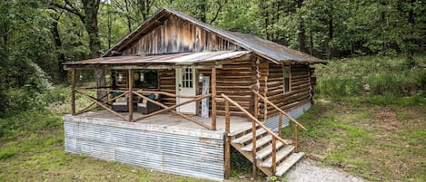 A rustic cabin with a porch, wooden steps, and a gravel path.
