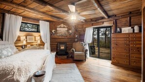 Une chambre à coucher située dans une cabane en rondins, avec un lit, une cheminée, un fauteuil et une commode.