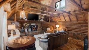 L’intérieur d’une cabane en rondins, avec une cheminée, un canapé en cuir, une table d’échecs et un téléviseur.