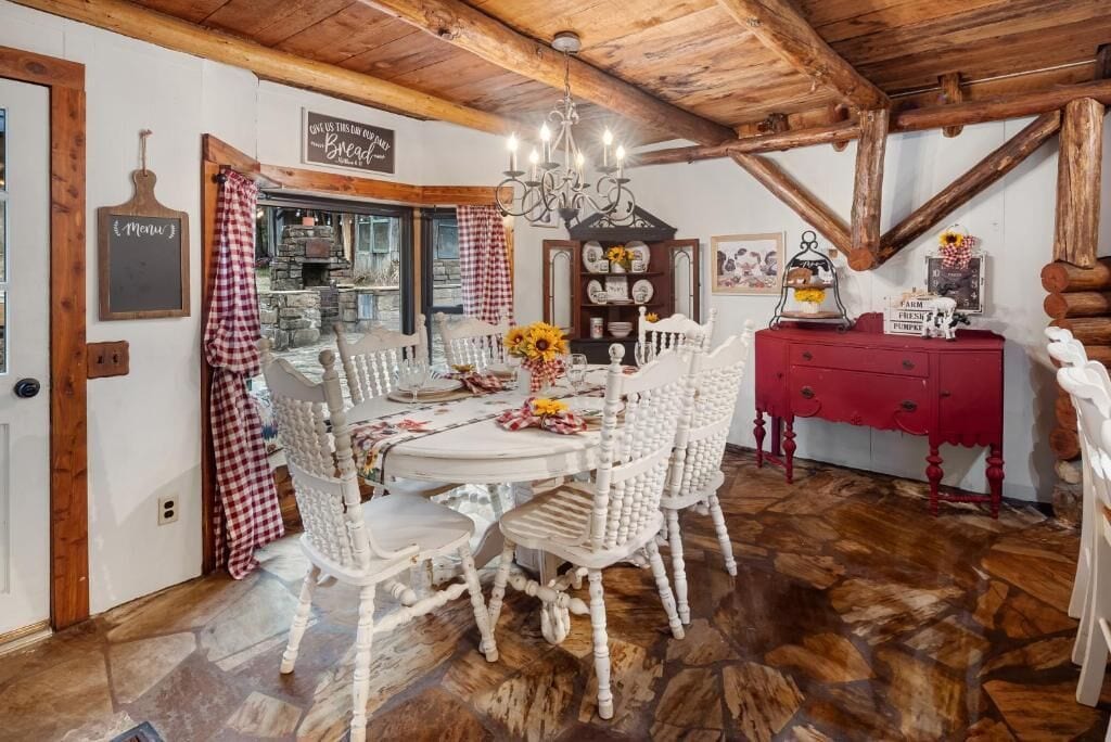 Ein rustikaler Essbereich mit Holzbalkendecke, einer Kristallleuchtre, weißen Korbstühlen, einem roten Schrank und einem Steinfußboden.