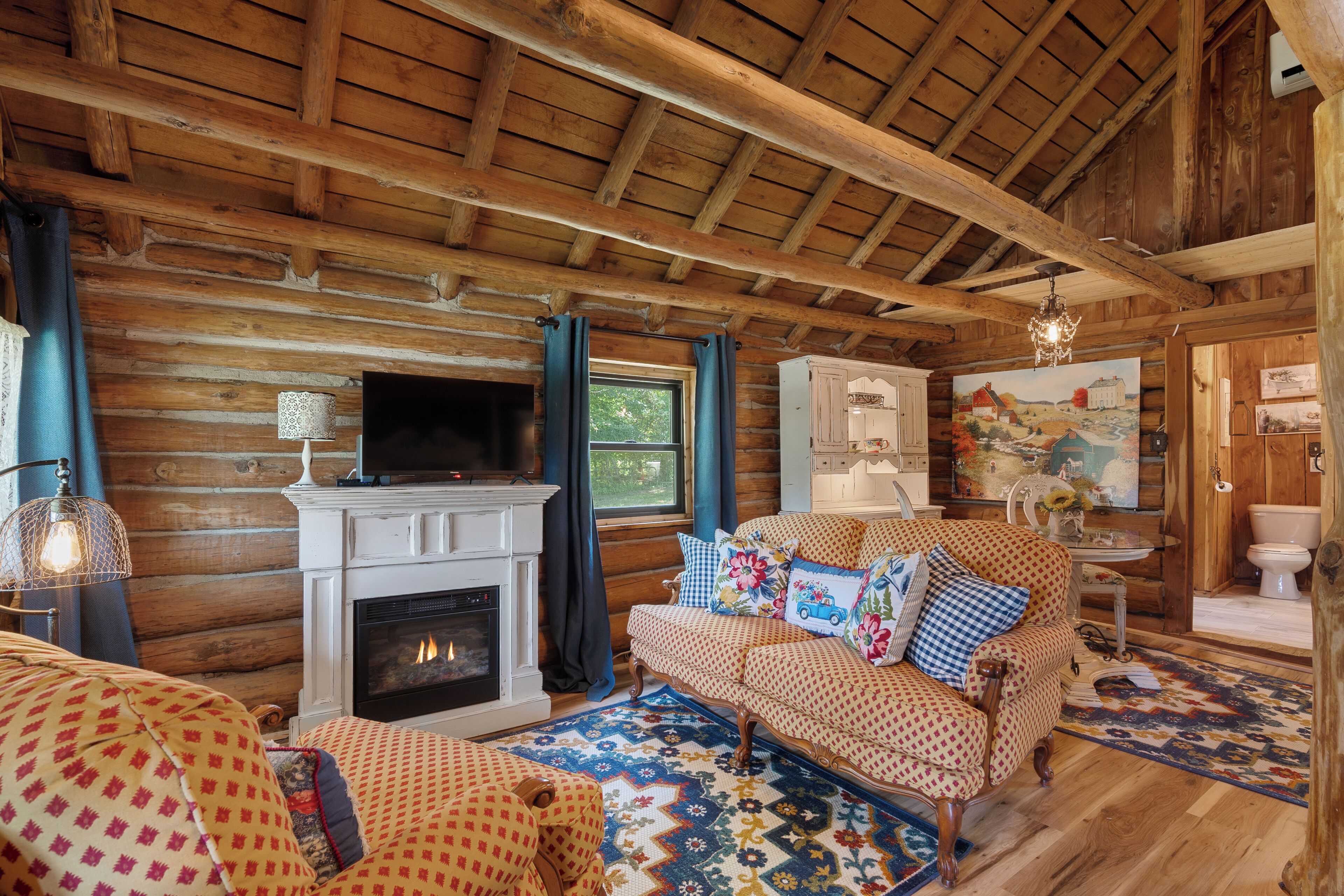 A log cabin interior with a fireplace, patterned sofa, and a painting on the wall.