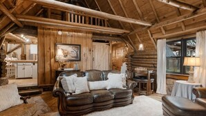 L’intérieur d’une cabane en rondins, avec un canapé en cuir, des murs en bois, une table à manger et un coin cuisine.