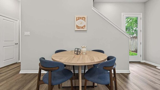 Un comedor con una mesa redonda de madera, cuatro sillas azules, un jarrón y un cartel motivacional en la pared.