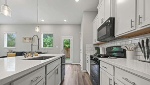 Una cocina moderna con armarios blancos, una isla central, electrodomésticos de acero inoxidable e iluminación colgante.