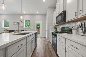 A modern kitchen with white cabinetry, a central island, stainless steel appliances, and pendant lighting.