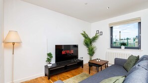 A modern living room with a flat-screen TV, a sofa, a floor lamp, and a window with a view. - Spacious 2BR Ground Floor Sleeps 5 Near Peterhead Harbour FREE Parking Fast WiFi (Aberdeenshire)