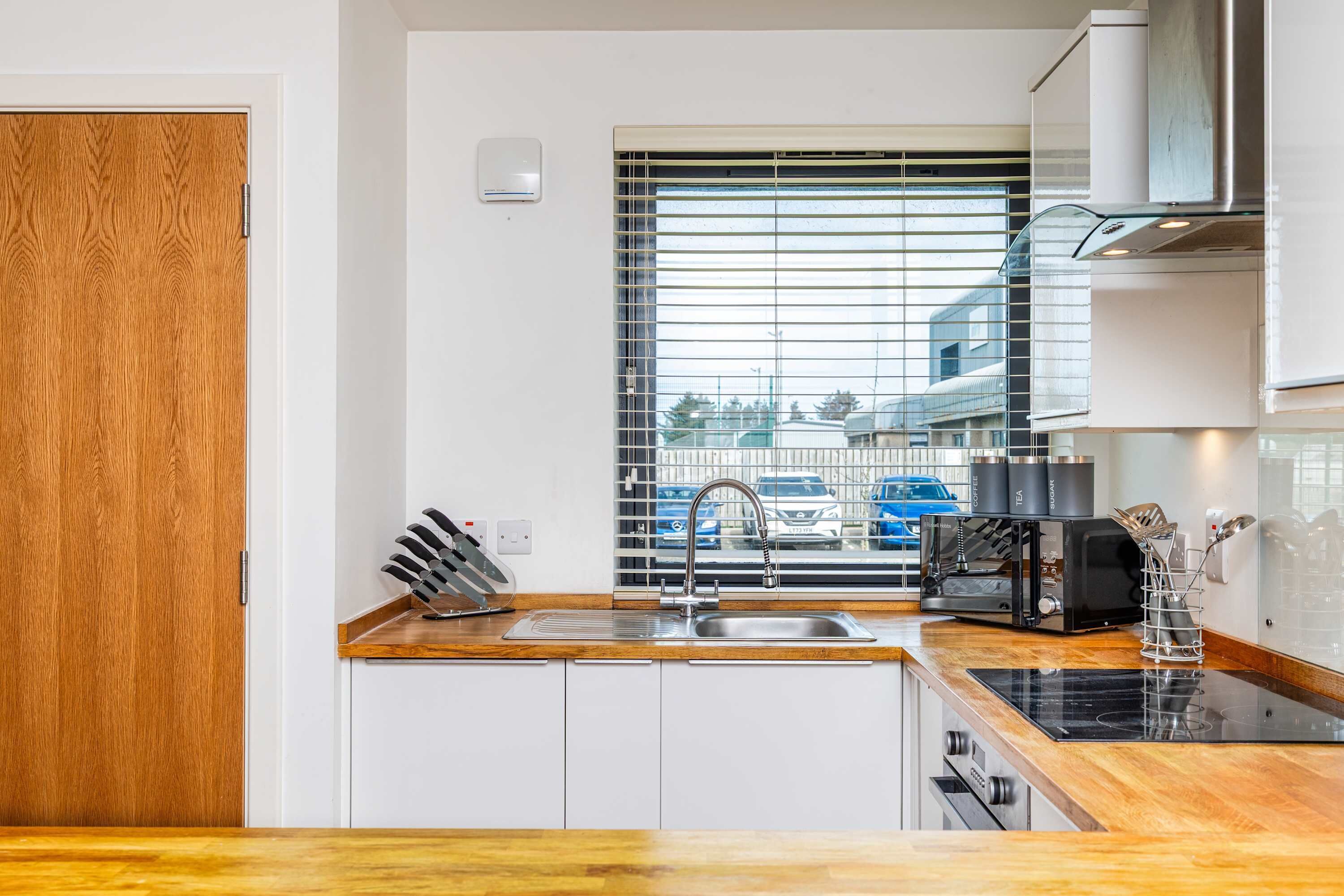 A modern kitchen with a wooden countertop, stainless steel sink, and a window with blinds.
