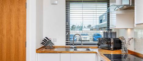A modern kitchen with a wooden countertop, stainless steel sink, and a window with blinds.