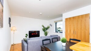 A modern living room with a grey sofa, a wooden dining table, and a TV displaying 'NETFLIX'. - Spacious 2BR Ground Floor Sleeps 5 Near Peterhead Harbour FREE Parking Fast WiFi (Aberdeenshire)