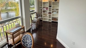 A room with a wooden floor, a window with a view of greenery, a bookshelf, and a chair. - Spacious 4-bedroom apartment At IMG Academy (Bradenton)
