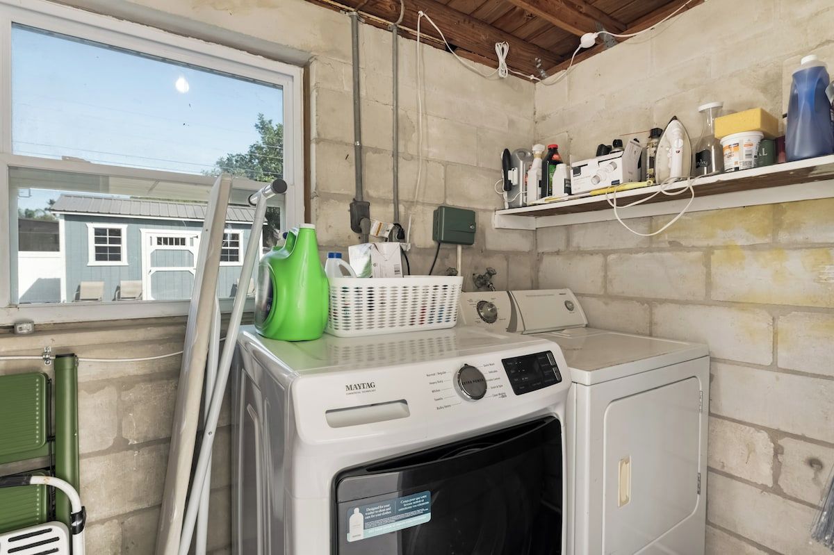 Une buanderie équipée d’un lave-linge et d’un sèche-linge Maytag, d’un panier à linge vert et d’une étagère contenant divers produits de nettoyage.