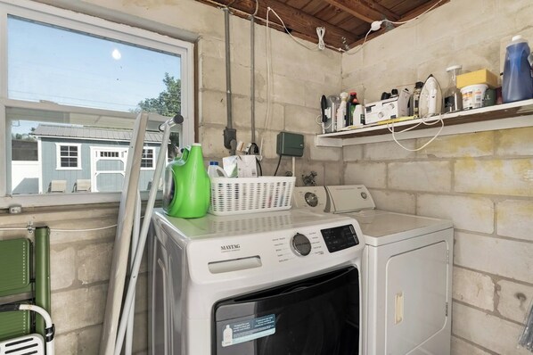 A laundry room with a Maytag washer and dryer, a green laundry basket, and a shelf with various cleaning supplies. - Beachside 3BR w/ New Hot Tub & Huge Backyard (Largo)