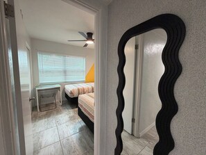 Ein Schlafzimmer mit einem Bett, einem kleinen Tisch, einem Sessel, einem Deckenventilator und einem Fenster mit Jalousien.