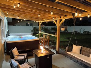 A covered outdoor patio with a hot tub, seating area, and a fire feature. - Beachside 3BR w/ New Hot Tub & Huge Backyard (Largo)