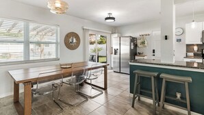 A modern kitchen with a dining area, a bar counter, and a large window. - Beachside 3BR w/ New Hot Tub & Huge Backyard (Largo)