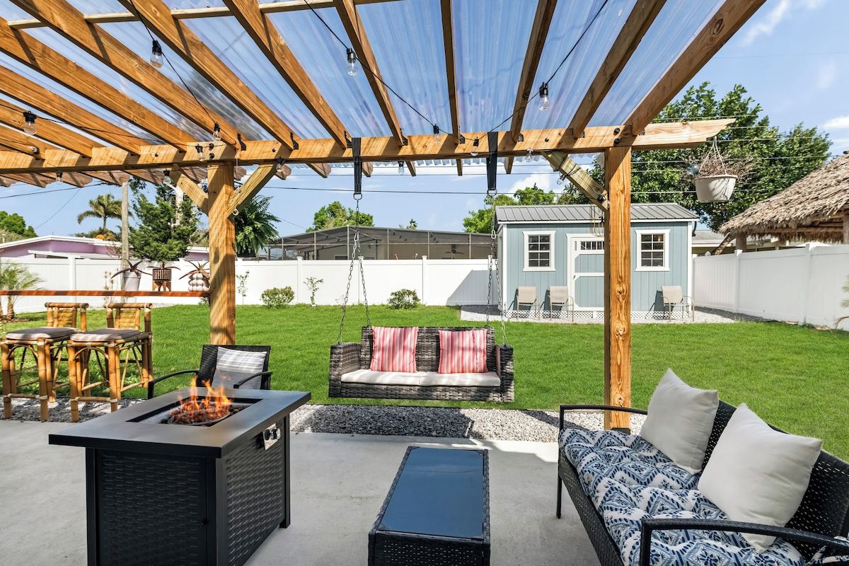 An outdoor patio area with a fire pit, seating, and a pergola structure.