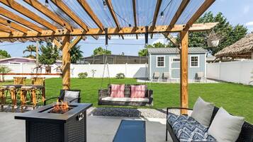 An outdoor patio area with a fire pit, seating, and a pergola structure.