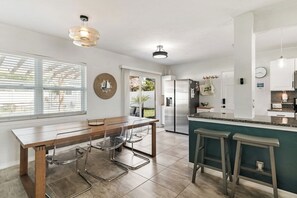 Eine moderne Küche mit Essbereich, ausgestattet mit einem Holztisch, Metallstühlen und einer Bar inklusive Sitzhocker.