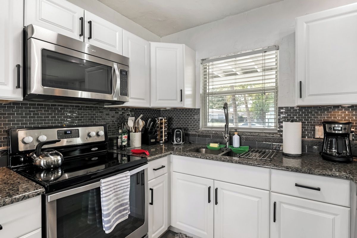 A modern kitchen with white cabinets, a stainless steel microwave, a gas stove, and a window with blinds.