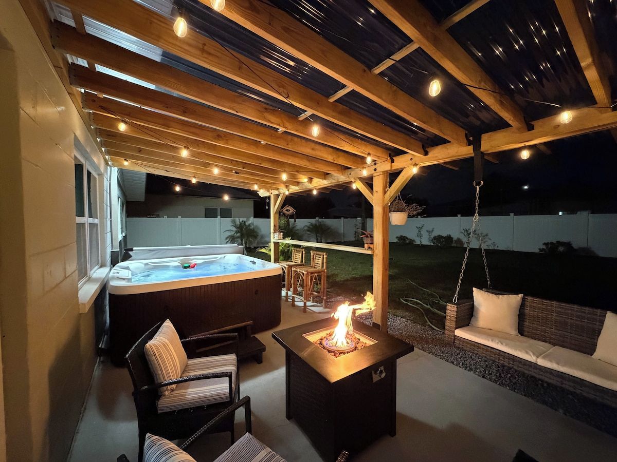 An outdoor patio area with a hot tub, seating, and a fire feature.