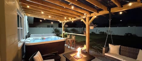 En udendørs patio med jacuzzi, siddepladser og bålsted.
