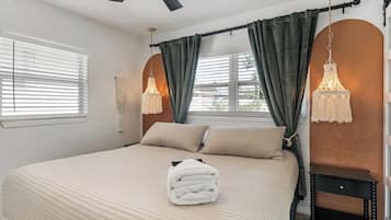A bedroom with a bed, a ceiling fan, two bedside lamps, and a window with curtains.