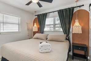 A bedroom with a bed, a ceiling fan, two bedside lamps, and a window with curtains. - Beachside 3BR w/ New Hot Tub & Huge Backyard (Largo)