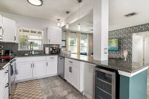 A modern kitchen with white cabinetry, a granite countertop, and a built-in dishwasher. - Beachside 3BR w/ New Hot Tub & Huge Backyard (Largo)