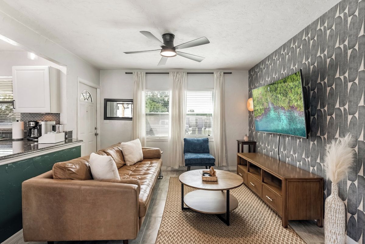 A modern living room with a sofa, a coffee table, a blue armchair, a TV, and a ceiling fan.