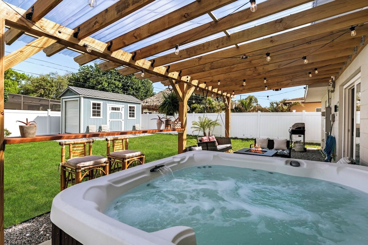 A hot tub under a wooden pergola with a clear view of a backyard, including a barbecue area and a small shed.