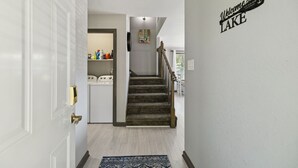A hallway with a carpeted staircase, a laundry room, and a wall sign that reads 'Welcome to the LAKE.' - Lakeside Escape (Dover)