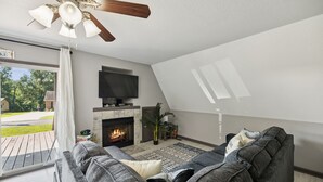 A living room with a fireplace, a sofa, a television, and a ceiling fan. - Lakeside Escape (Dover)