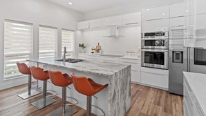 Een moderne keuken met een marmeren eiland, roestvrijstalen apparatuur en oranje barkrukken.