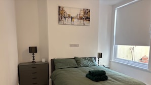 A bedroom with a bed, a nightstand, a lamp, a painting, and a window. - Coastal Retreat, Rhos-on-Sea, 1-Min Walk to Beach (Rhos on Sea)