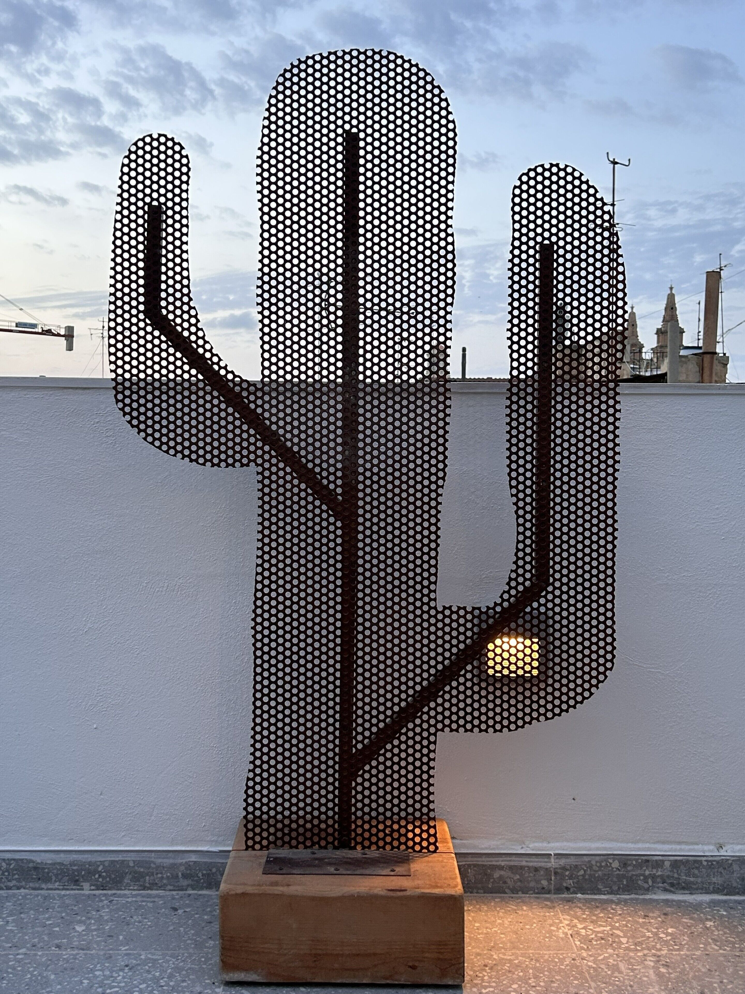 Une sculpture de cactus avec un motif en treillis métallique, posée sur un socle en bois.