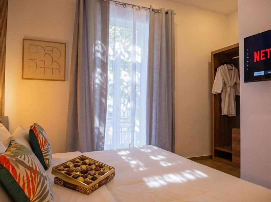 A hotel room with a bed, a tray of chocolates, a robe hanging, and a TV displaying the Netflix logo.