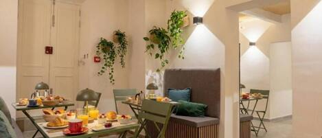 A dining area with a table set for breakfast, a sofa, and hanging plants.