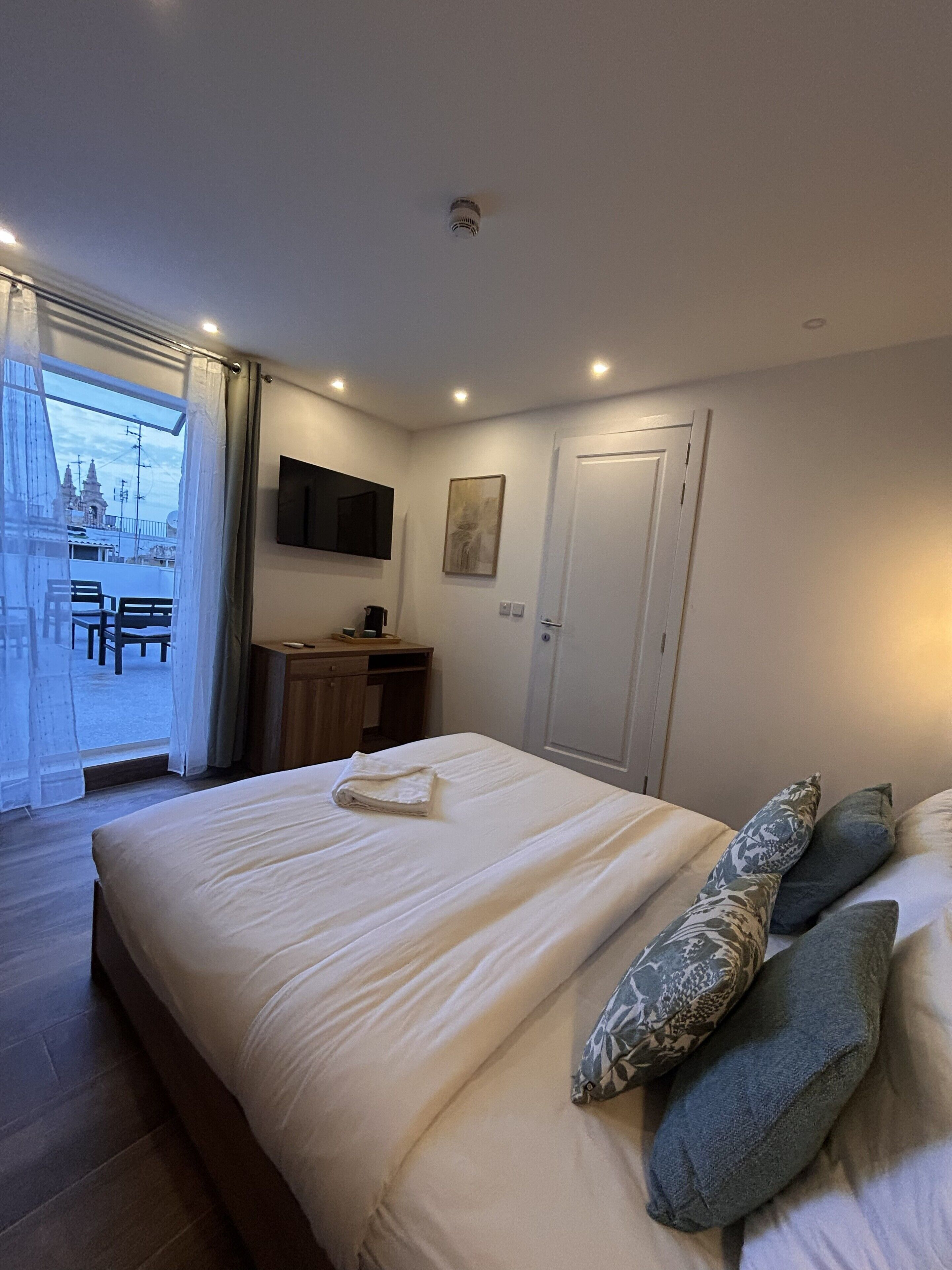 A bedroom with a bed, a desk, a chair, a TV, and a door.