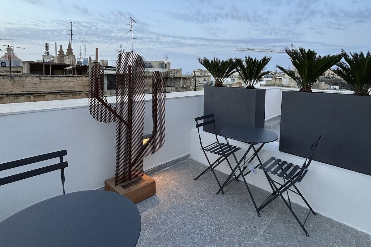 An outdoor seating area with a table and chairs, a decorative metal sculpture, and a view of the cityscape.