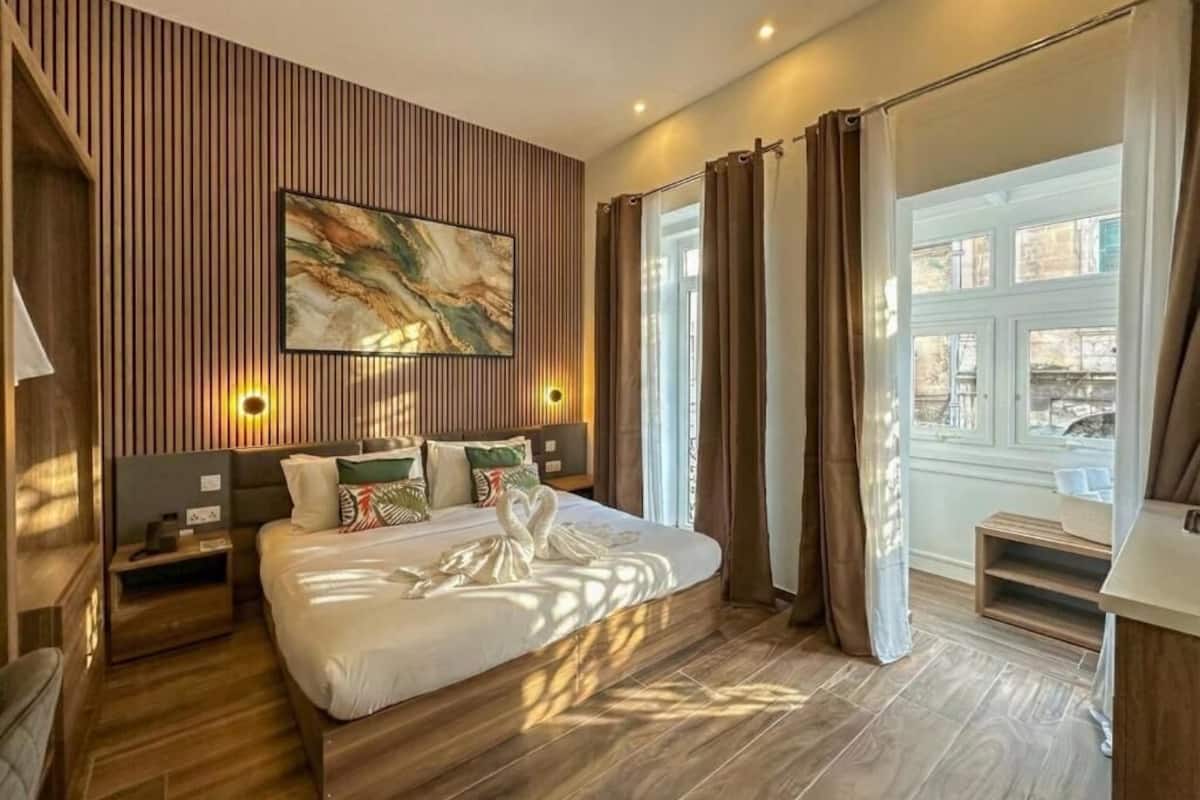A modern hotel room with a large bed, wooden paneling, a painting, and a view through curtains.