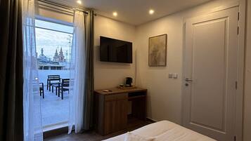 A hotel room with a bed, a desk, a TV, a door, and a window with curtains.