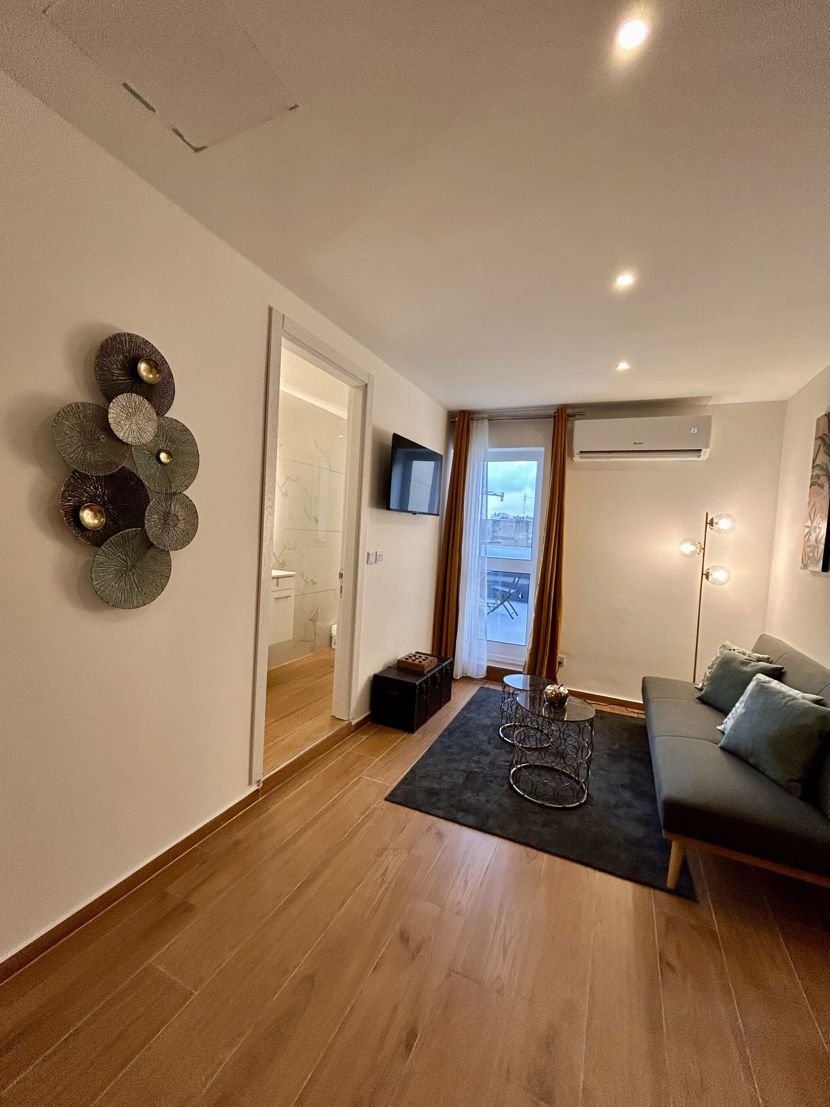 Una sala de estar moderna con piso de madera, un sofá gris, una mesa de centro y un televisor montado en la pared.