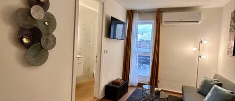 Una sala de estar moderna con piso de madera, un sofá gris, una mesa de centro y un televisor montado en la pared.