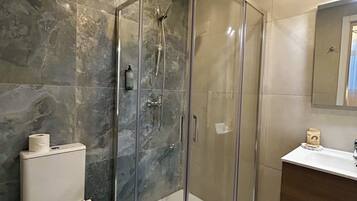 Un baño moderno con ducha de vidrio, inodoro y tocador con espejo.